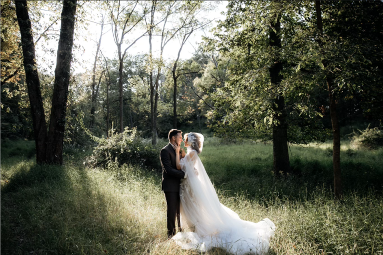 Bride and groom kiss in woodland meadow